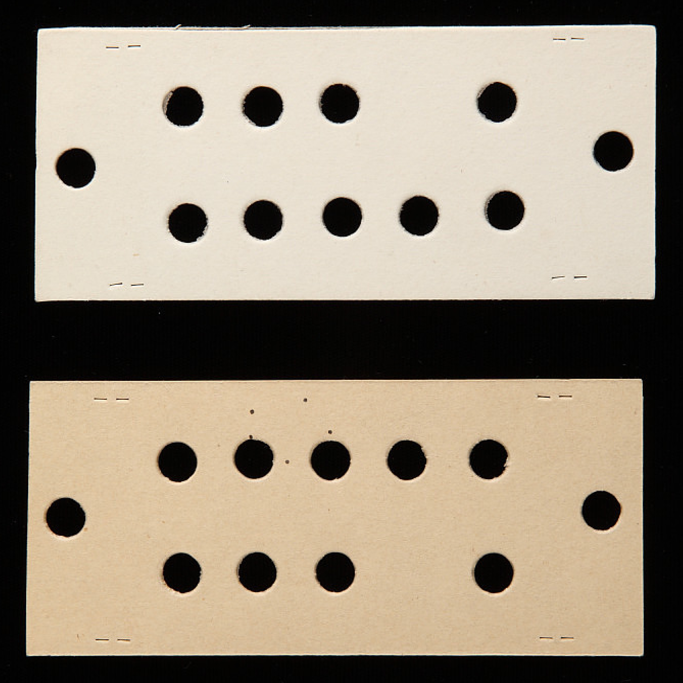 Two punch cards. One card is white on both sides. The other is tan on one side and grayish-brown on the other. Each card has round holes at both ends, as well as two rows of round holes in the middle. There also are cuts in the top and bottom edges.